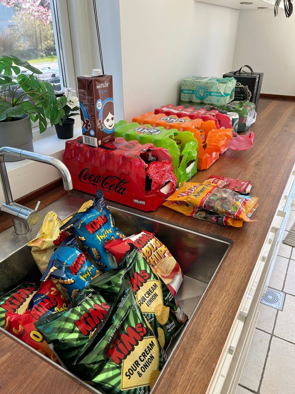 Crates of Coke and Fanta on the worktop and a kitchen sink filled with bags of crisps